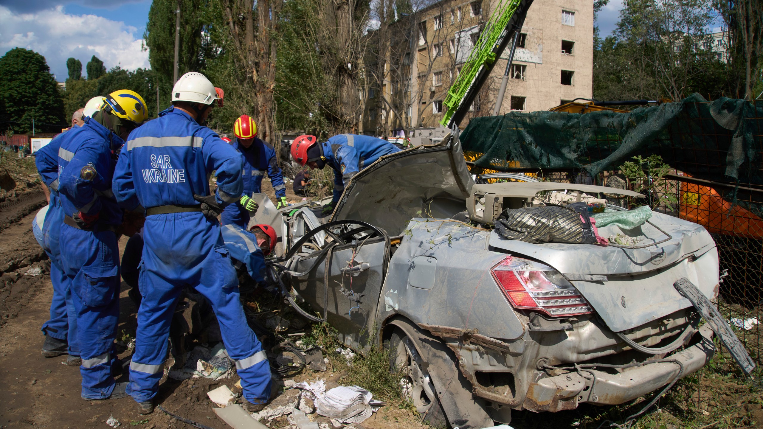 Emergency workers inspect a damaged car close to the multi-storey residential house that was ruined by a Russian missile Thursday night, killing 31 civilians including five children, in Kyiv, Ukraine, Friday, Aug. 1, 2025. (AP Photo/Efrem Lukatsky)