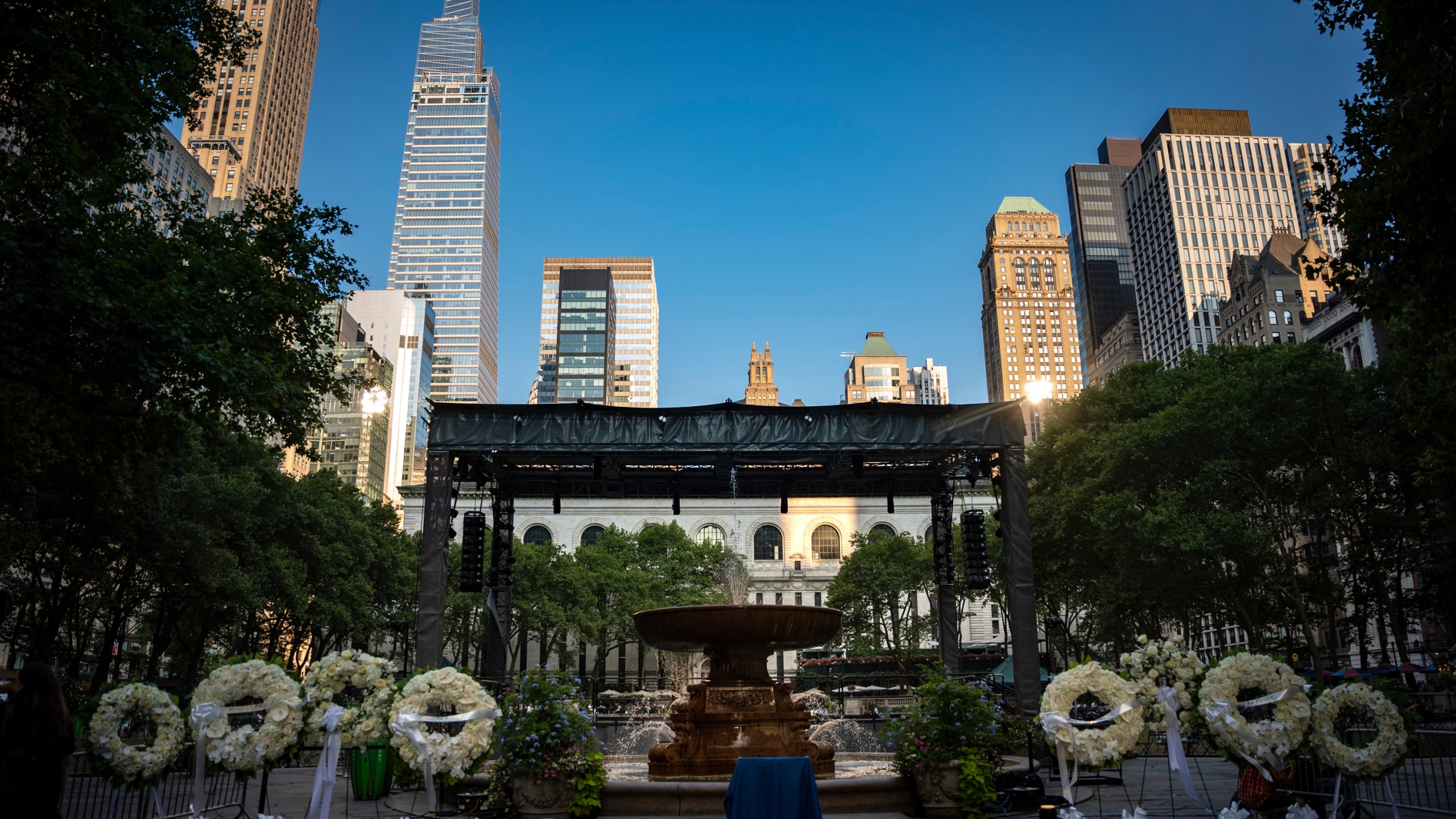 Flower wreaths with the words "Rest In Peace" stand at a vigil