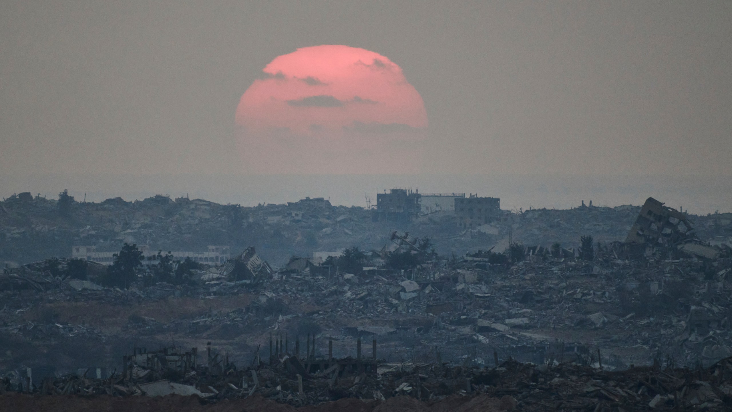 The sun sets behind buildings that were destroyed during the Israeli ground and air operations stand in the northern Gaza Strip as seen from southern Israel, Friday, Aug. 8, 2025. (AP Photo/Leo Correa)