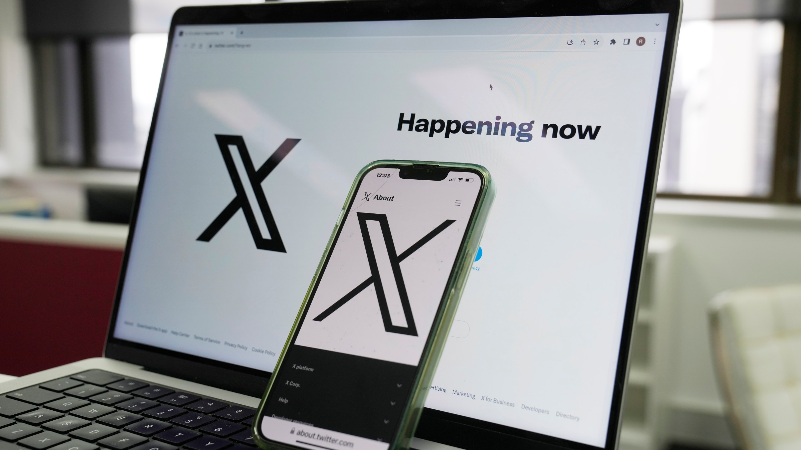 The opening page of X is displayed on a computer and phone