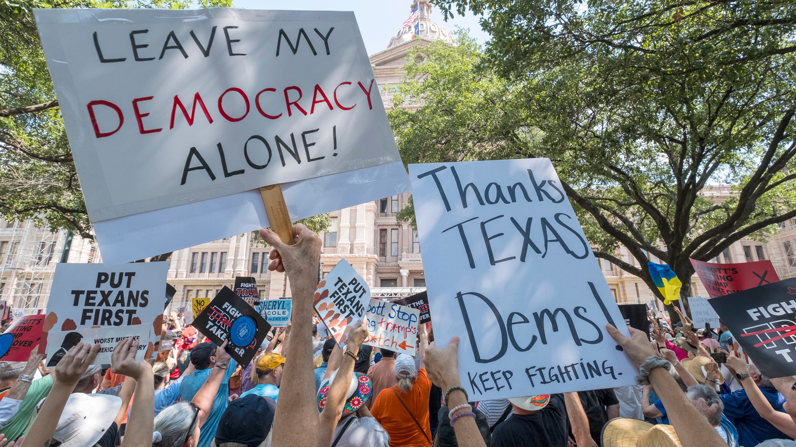 Protesters hold up signs reading LEAVE MY DEMOCRACY ALONE! and THANKS TEXAS DEMS! KEEP FIGHTING