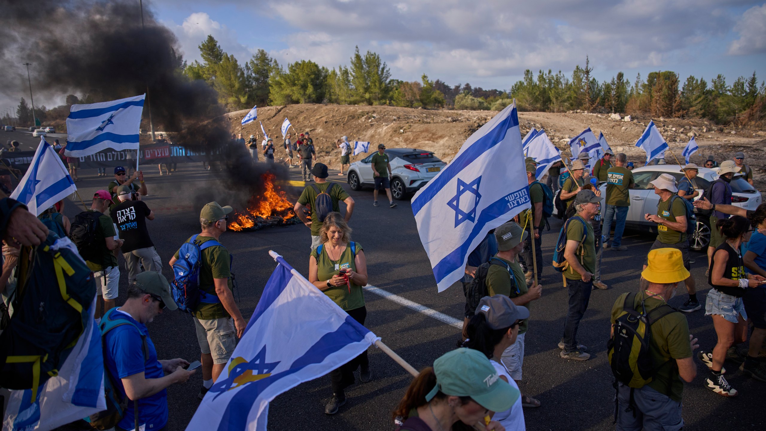 Demonstrators block a road during a protest demanding the immediate release of hostages held by Hamas and calling for the Israeli government to reverse its decision to take over Gaza City and other areas in the Gaza Strip, near Jerusalem, Israel, Sunday, Aug. 17, 2025. (AP Photo/Ohad Zwigenberg)