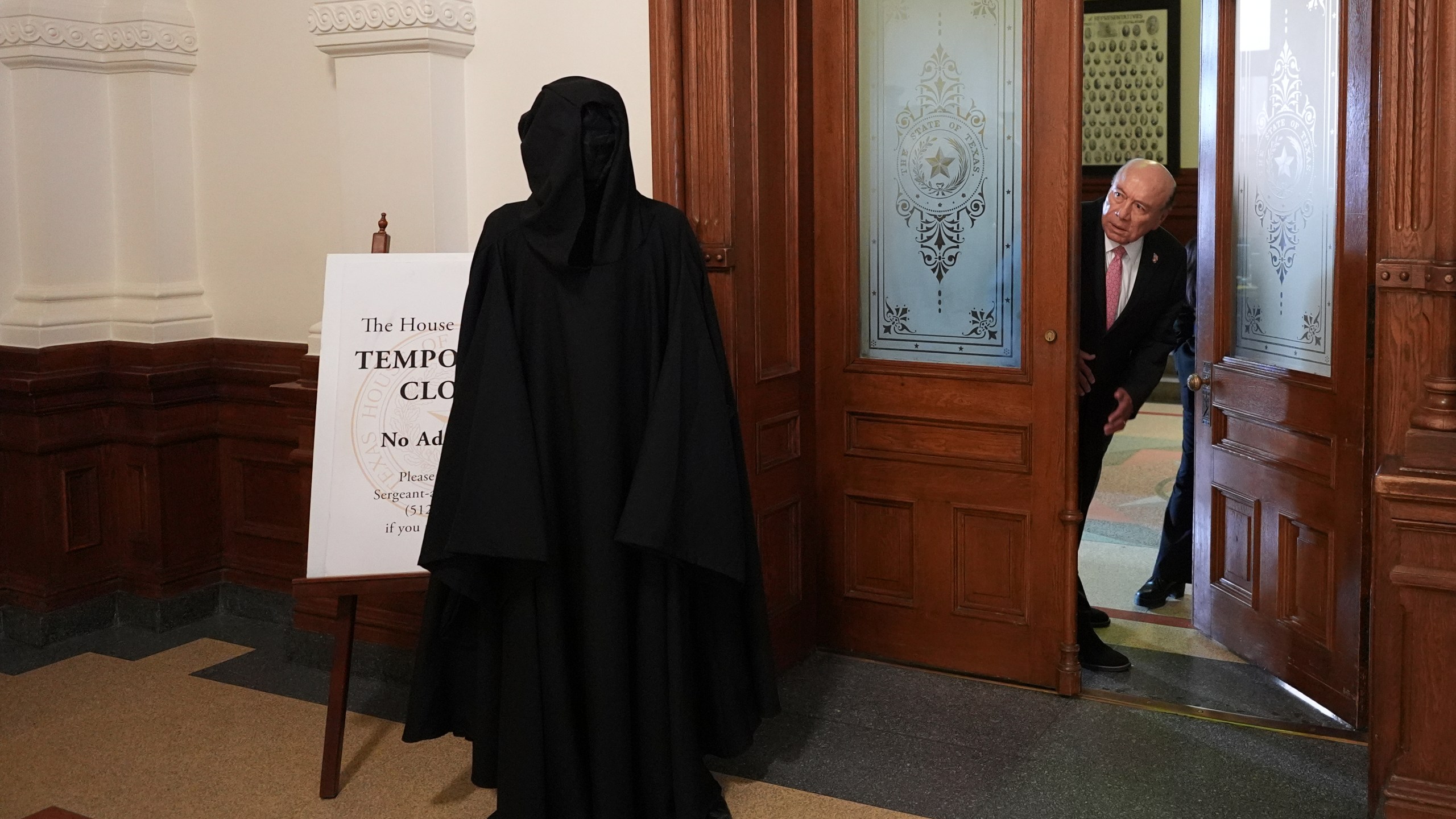 Texas state Sen. Juan "Chuy" Hinojosa, right, looks at a protester dressed as death standing outside of the House Chamber where Democratic Texas state Rep. Nicole Collier refuses to leave due to a required law enforcement escort, Tuesday, Aug. 19, 2025, in Austin, Texas. (AP Photo/Eric Gay)