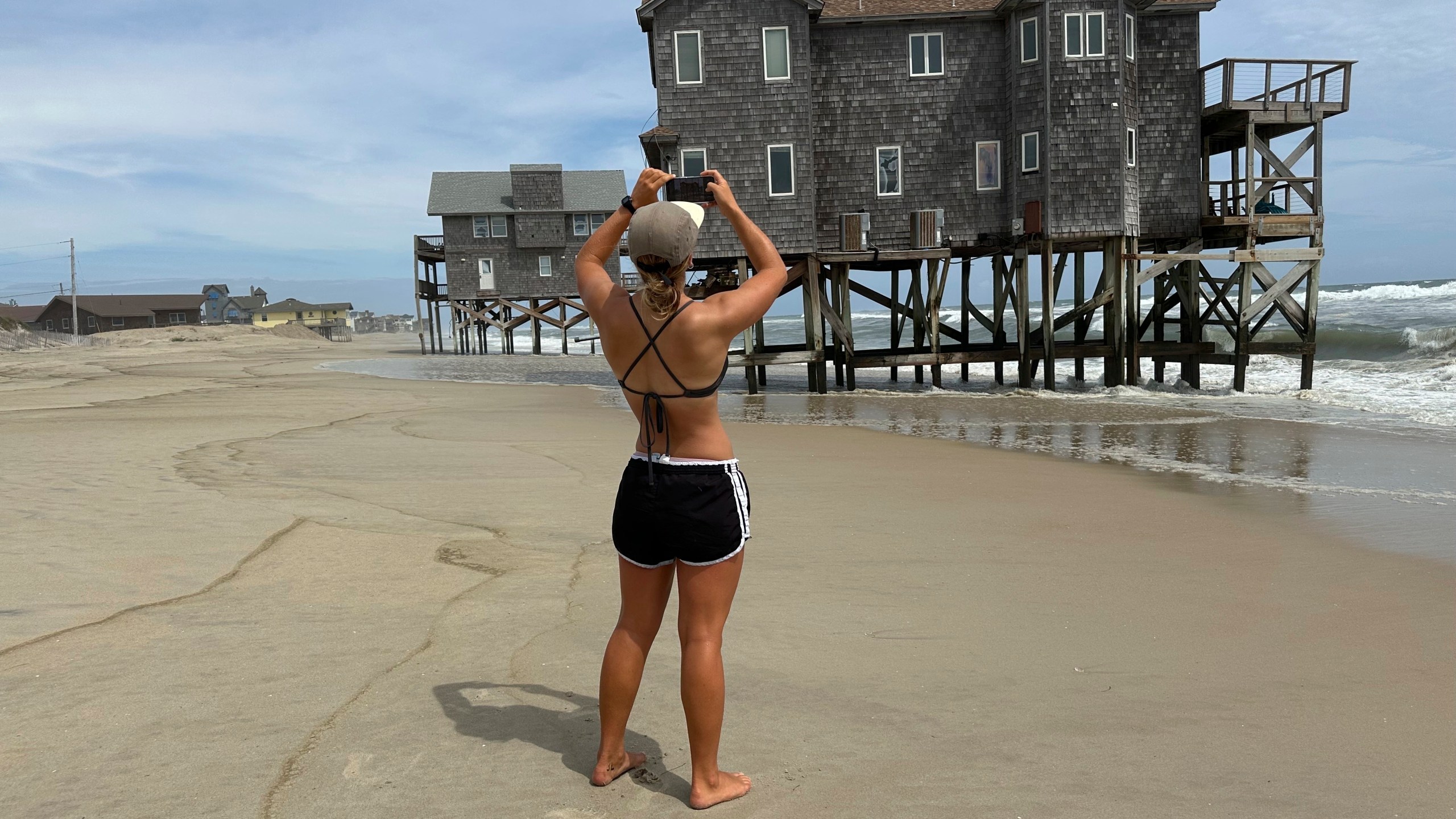 Maggie Ford takes a photo of a teetering stilt house being pummeled by waves from Hurricane Erin in Rodanthe, N.C., on Wednesday, Aug. 20, 2025. (AP Photo/Allen G. Breed)