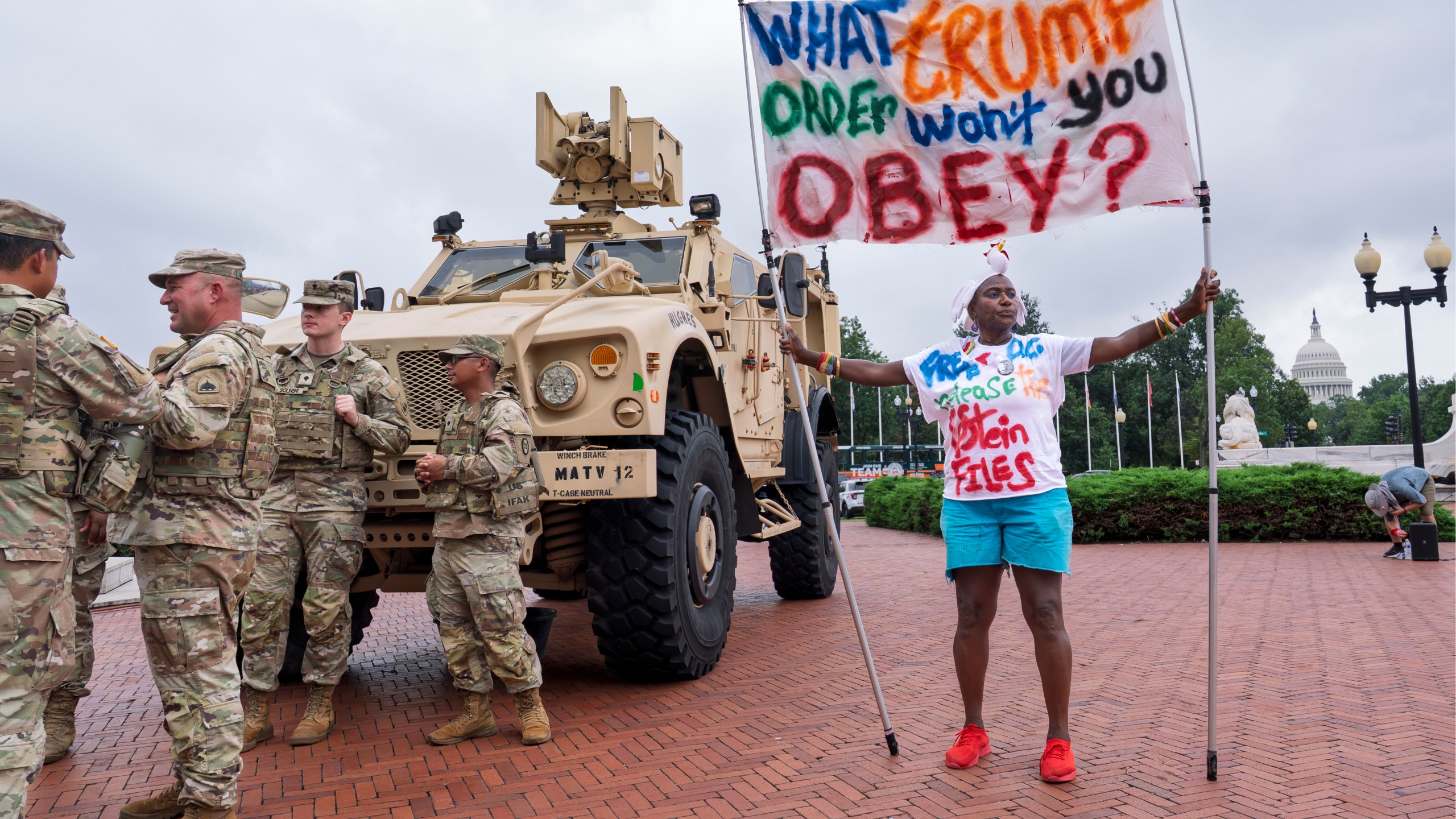 Nadine Seiler of Waldorf, Md., displays her banner as protesters, police, and National Guard troops congregate at the entrance to Union Station in Washington, Wednesday, Aug. 20, 2025. (AP Photo/J. Scott Applewhite)