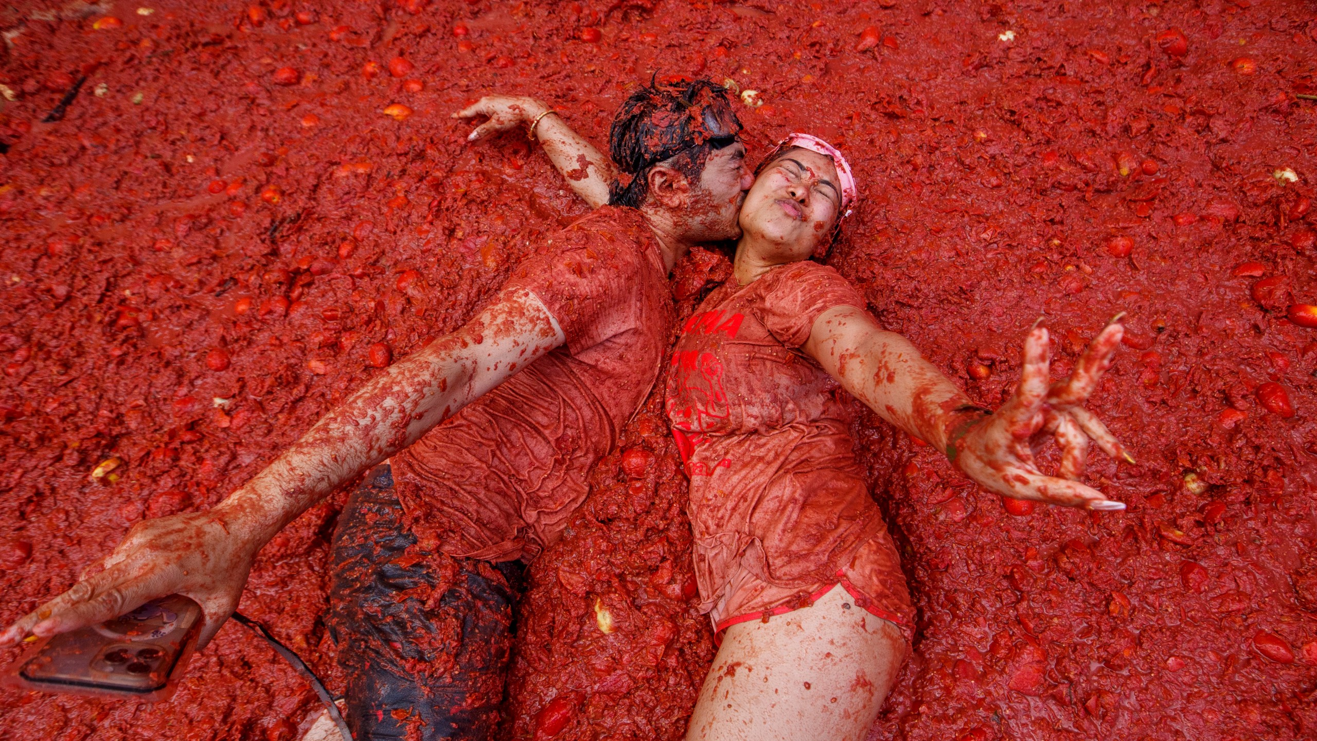 A couple kisses over a puddle of tomatoes during the annual "Tomatina" tomato fight fiesta, in the village of Bunol near Valencia, Spain, Wednesday, Aug. 27, 2025. (AP Photo/Alberto Saiz)
