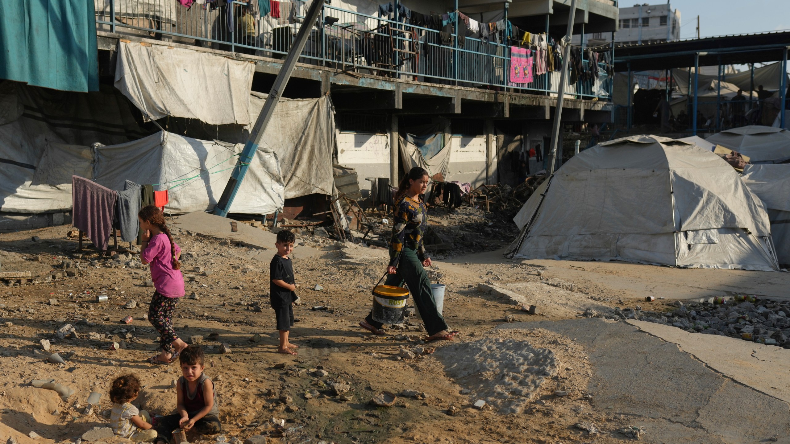 A woman carries buckets as she walks past tents
