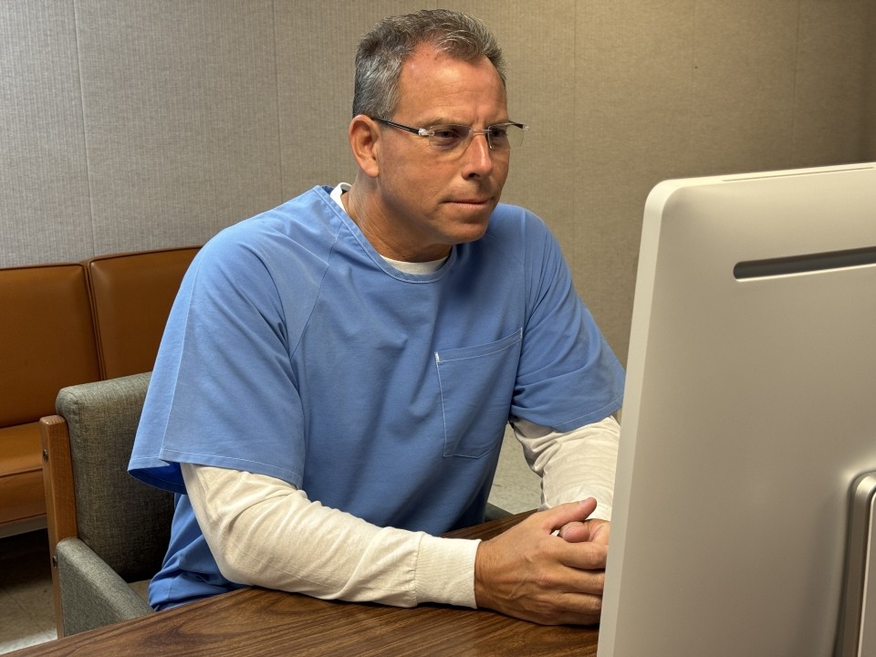 Erik Menendez with gray hear before a computer, wearing prison clothes.