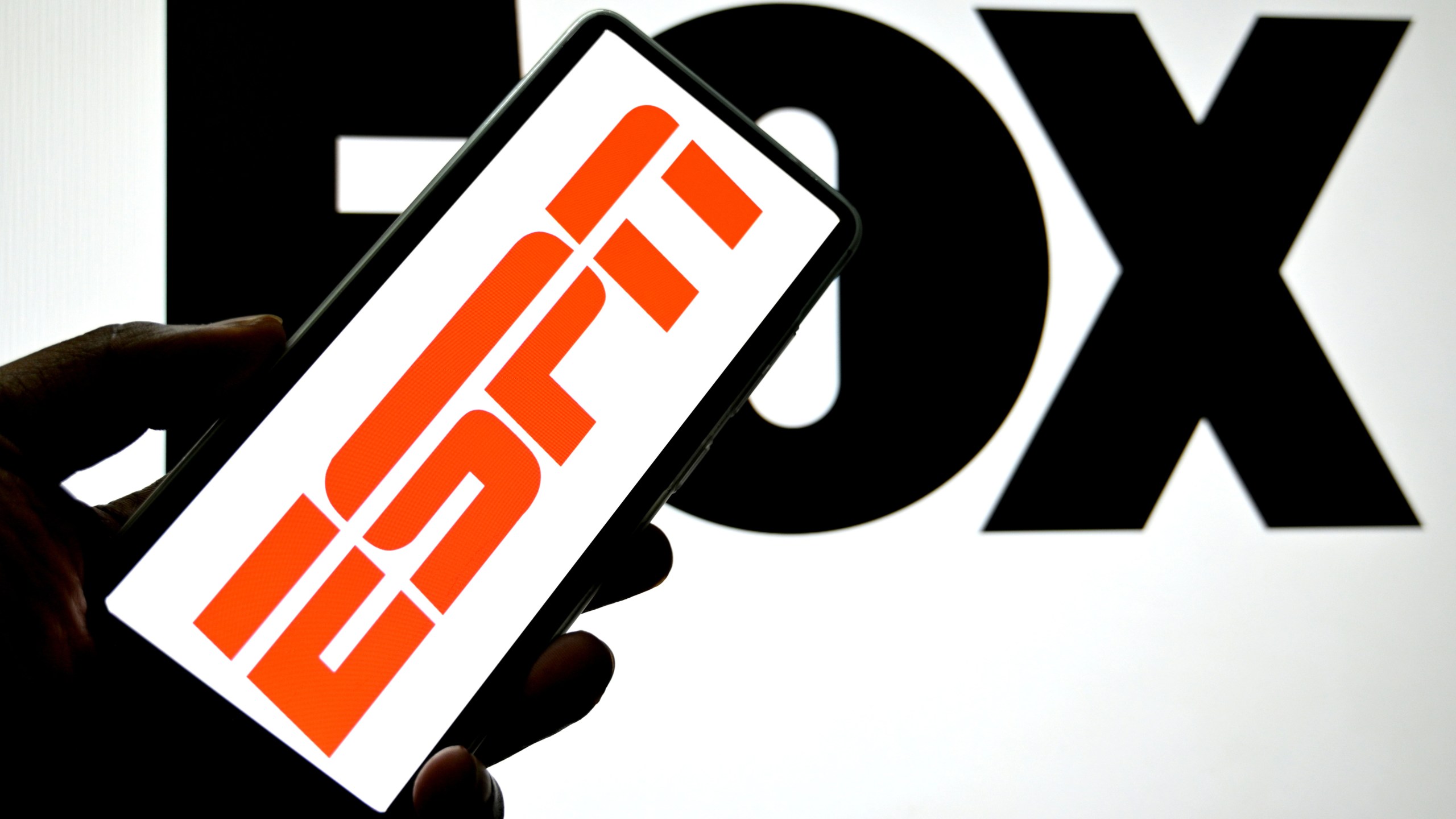 In this photo illustration, an ESPN logo is seen displayed on a smartphone with a FOX logo in the background