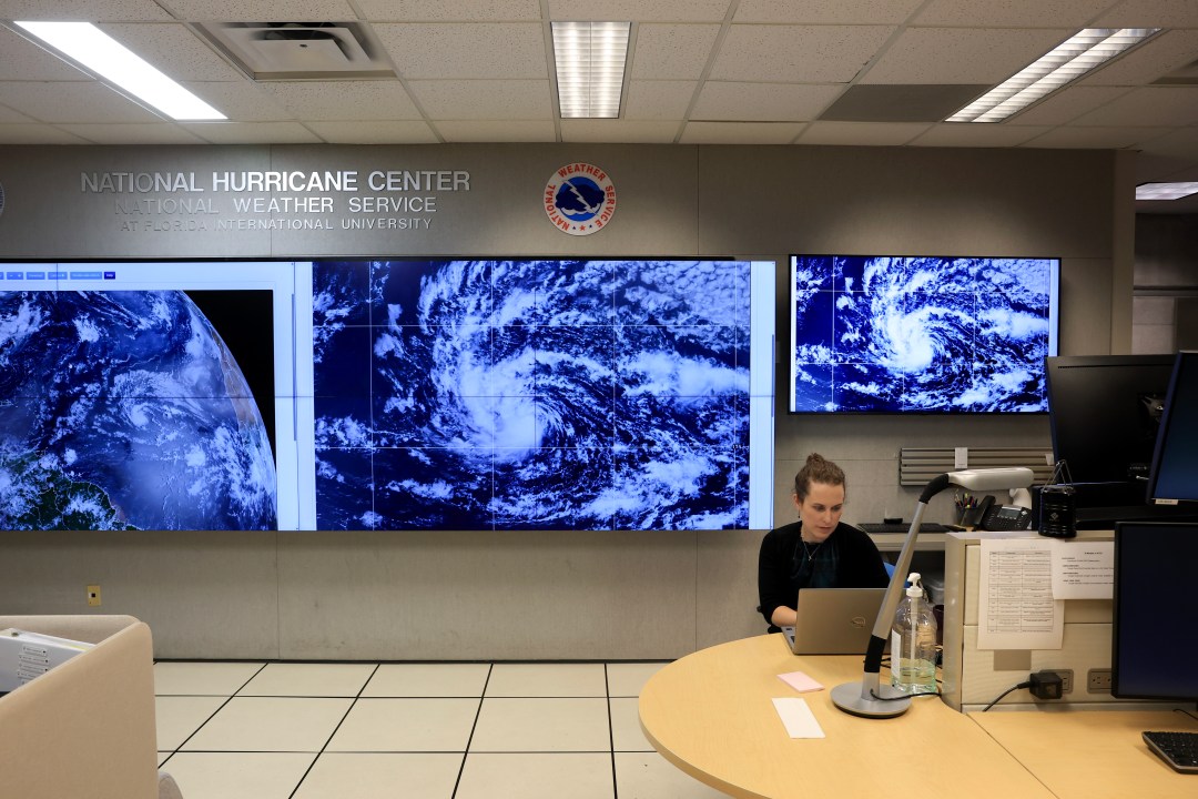 woman works at computer in front of screens showing a hurricane