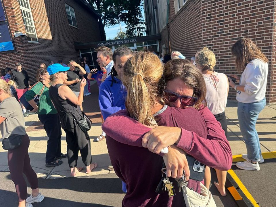 Two women hug outside of Annunciation Church in Minneapolis, Minnesota after reported school shooting