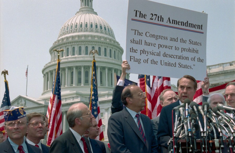This 1990 photo shows Republican Senate leader Sen. Robert Dole (R) speaks at a rally in front of the U.S. Capital in support of a proposed amendment to the Constitution that would have banned desecration of the American flag. Looking on are Sen. Alfonse D'Amato (R-N.Y.) (C) and Sen. Phil Gramm (L), R-Texas.