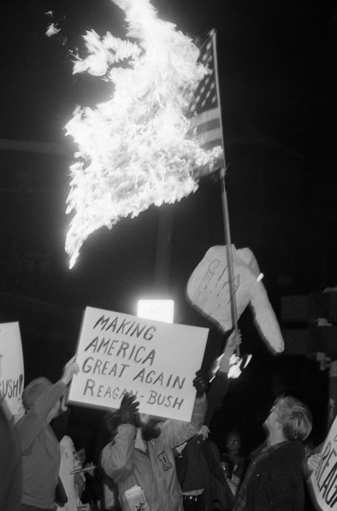 October 30, 1981: An American flag is burned by protesters as Vice President George Bush spoke nearby at Massachusetts Institute of Technology. Placard, foreground, backs President Reagan and Vice President Bush.