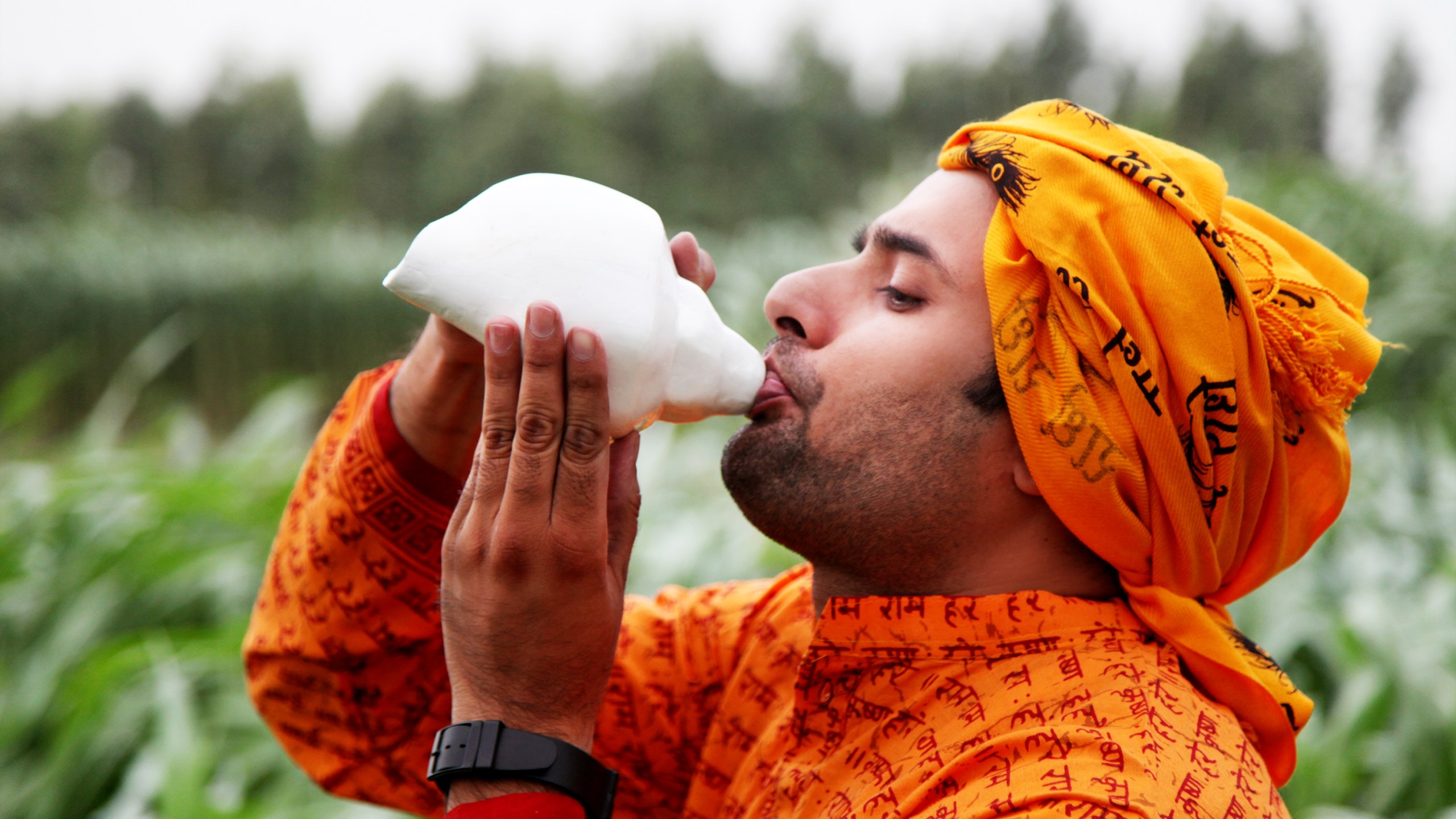 man blowing into a conch shell outdoors
