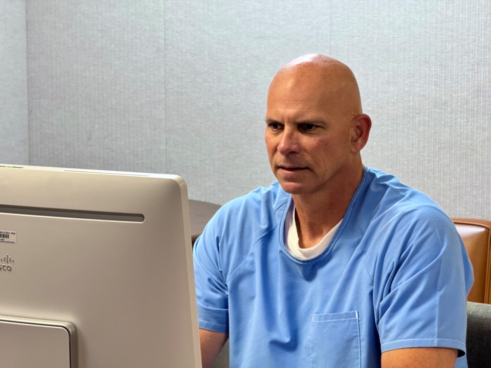 Lyle Menendez in prison clothing before computer monitor