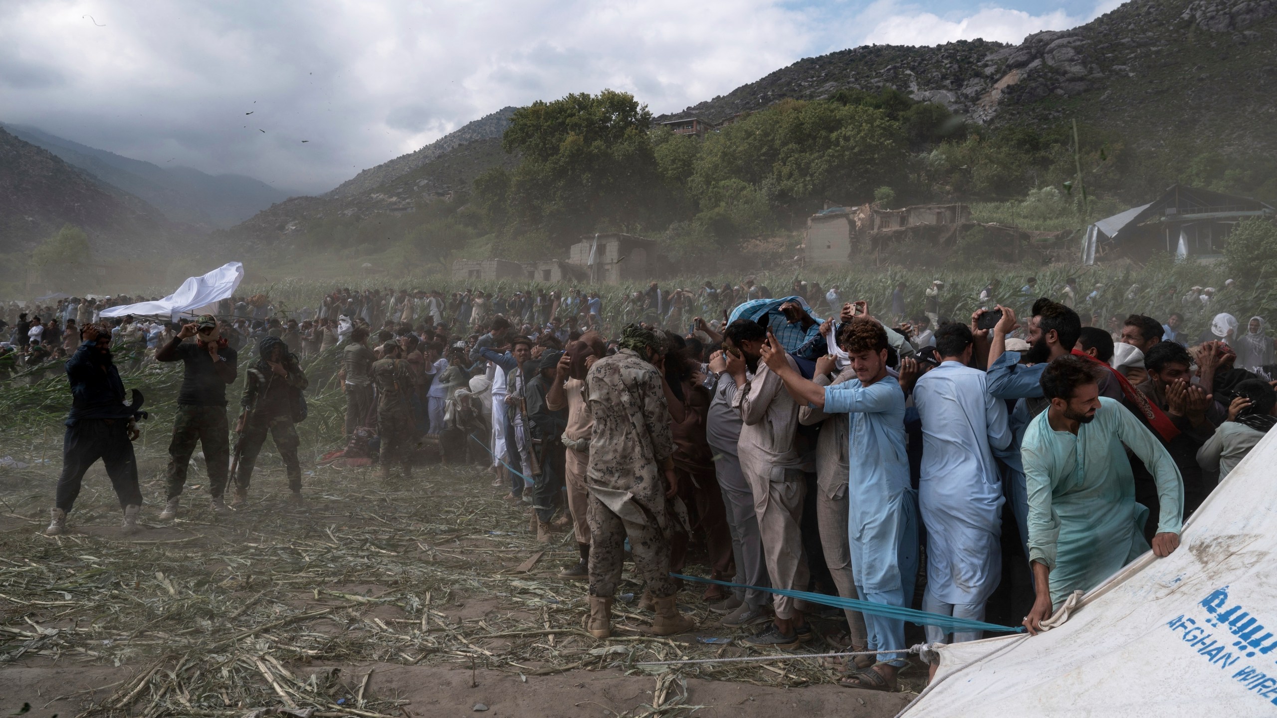 Residents and Taliban soldiers shield themselves from the wind of a helicopter taking off as efforts continue after Sunday night's powerful 6.0-magnitude earthquake that struck several provinces, in Kunar province, eastern Afghanistan, Tuesday, Sept. 2, 2025. (AP Photo/Nava Jamshidi)