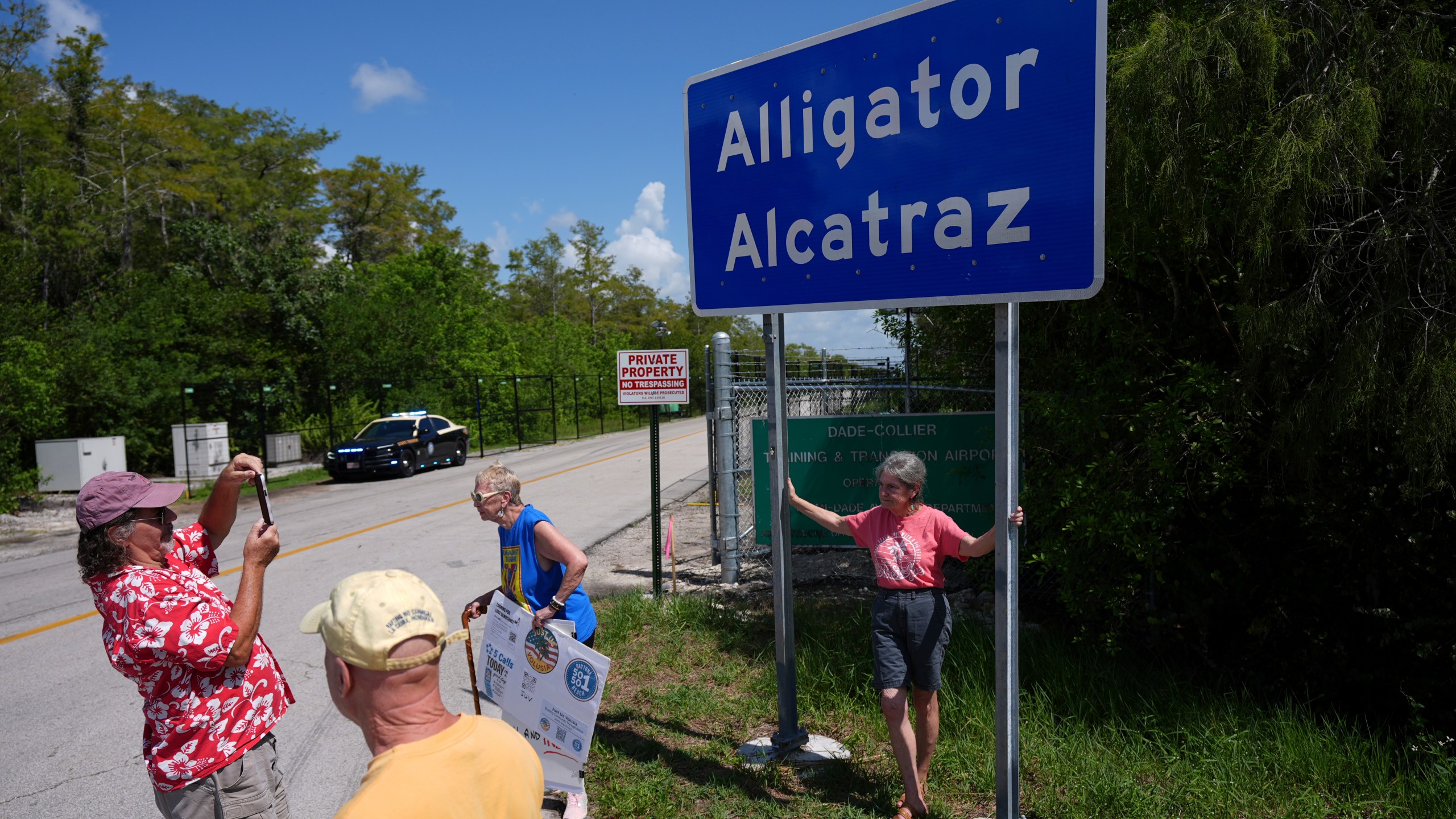 People take pictures in front of a sign reading "Alligator Alcatraz" as passerby, some opposed, some in support, visit the entrance to an immigration detention center in the Florida Everglades, Thursday, Aug. 28, 2025, in Collier County, Fla. (AP Photo/Rebecca Blackwell)