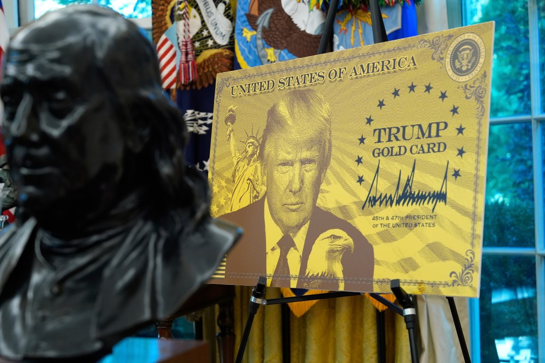 A gold poster with President Donald Trump's face on it that says "Trump Gold Card" is displayed in the Oval Office