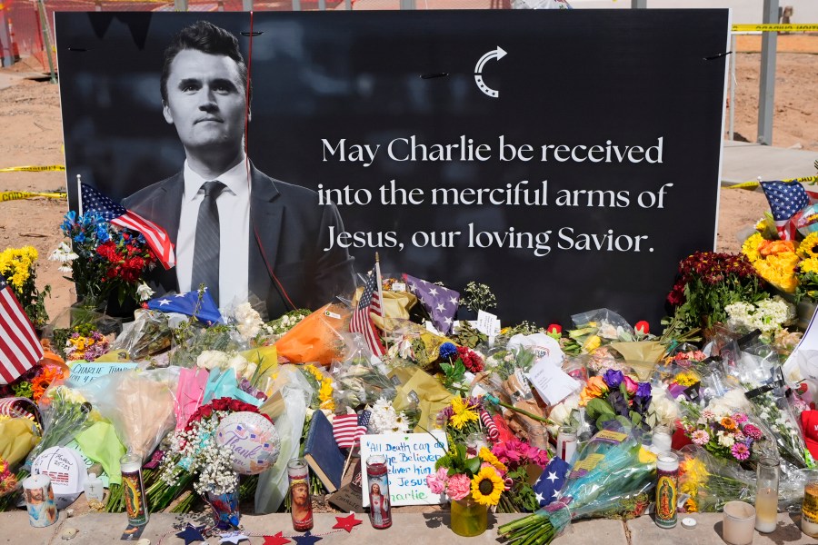 a memorial for Charlie Kirk with flowers and a sign reading MAY CHARLIE BE RECEIVED INTO THE MERCIFUL ARMS OF JESUS, OUR LOVING SAVIOR
