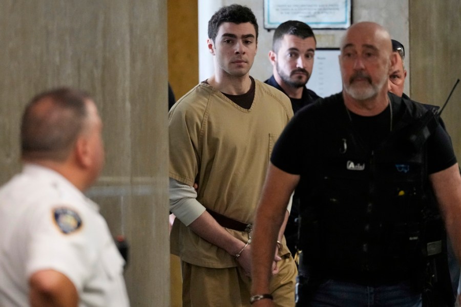 Luigi Mangione, wearing a beige jumpsuit and handcuffs, is escorted into court