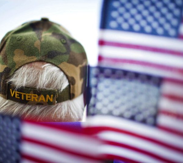 Photo of the back of a man's head with a hat that says "veterans" surrounded by American flags