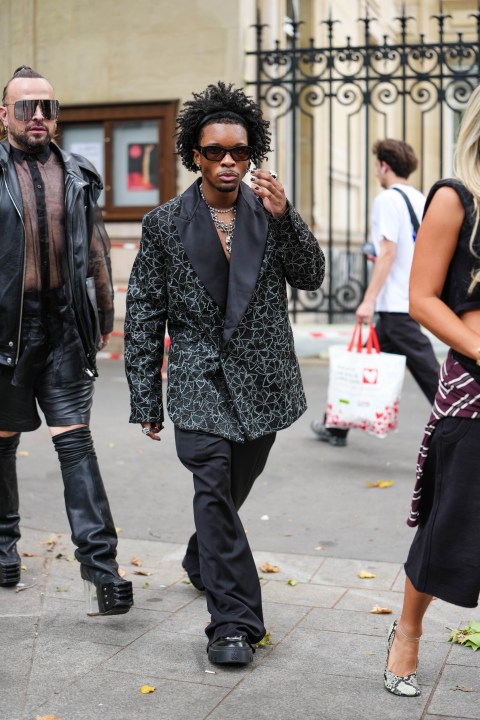 d4vd wears black Chanel sunglasses, diamond stud earrings, white gold diamond choker, silver Chrome hearts necklace, black silver floral beaded oversized Amiri blazer jacket, black baggy trouser pants, shiny black boots leather shoes, outside Amiri, during the Paris Fashion week