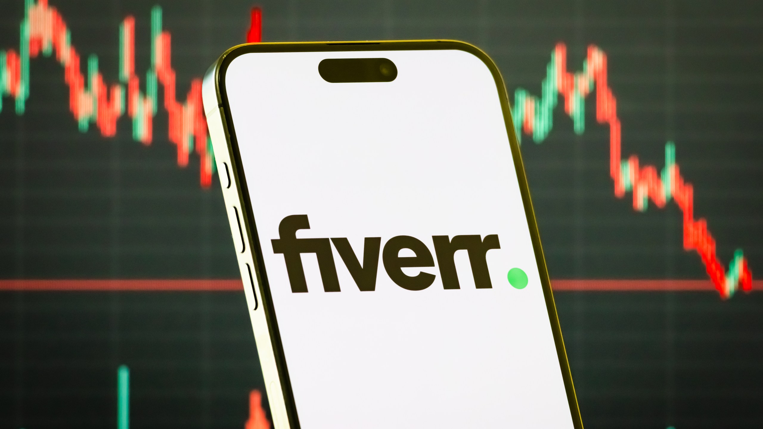 a smartphone displays the logo of Fiverr International Ltd. (NYSE: FVRR), an online marketplace for freelance services, in front of a screen showing the company's latest stock market chart