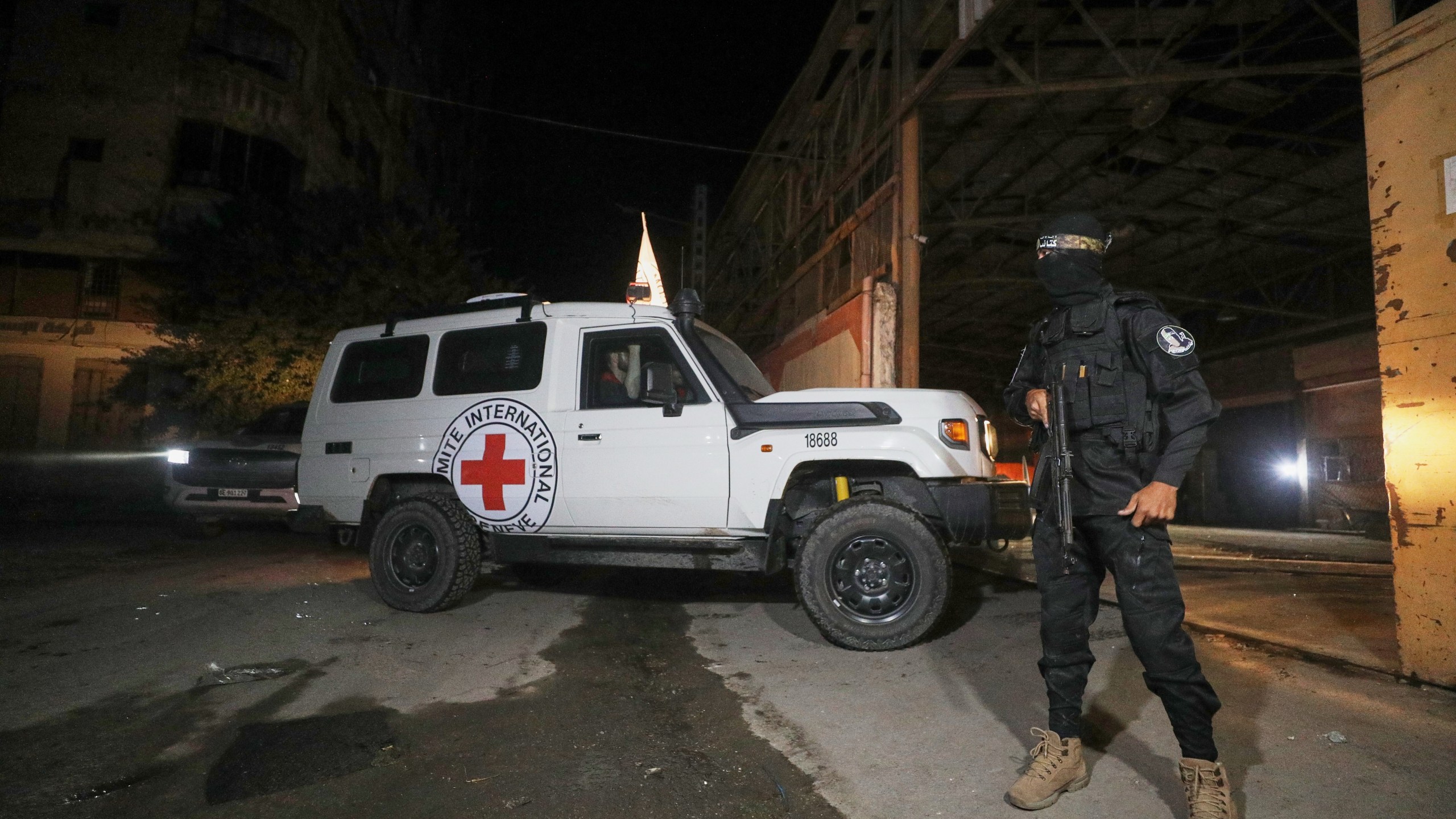 A gunman wearing the uniform of the al-Qassam Brigades, the military wing of Hamas, stands guard as Red Cross vehicles enter a warehouse allegedly to collect coffins containing the bodies of four deceased hostages, in Gaza City, Tuesday, Oct. 14, 2025. (AP Photo/Yousef Al Zanoun)