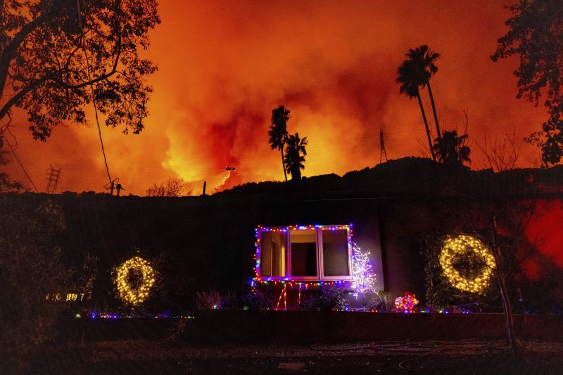 A helicopter drops water on the Palisades fire behind a home with Christmas lights in Mandeville Canyon on Jan. 10 in Los Angeles.