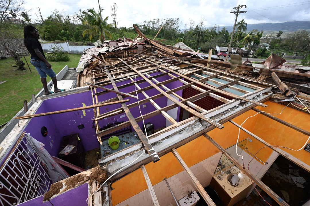 roof on the ground in Jamaica, person surveys damage
