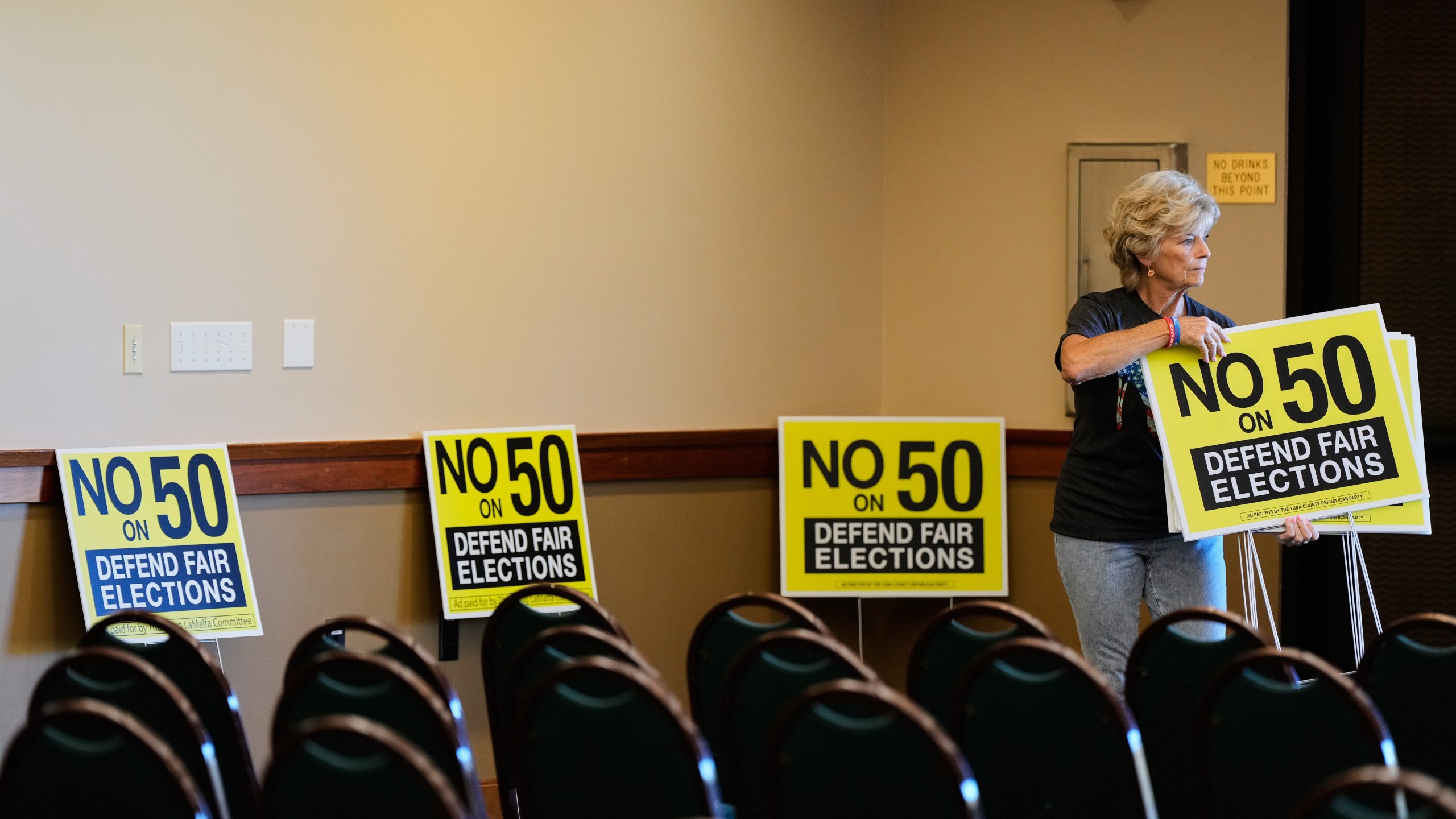 Brenda Haynes places signs throughout a conference room before a No on Prop 50 rally in Redding, Calif., Tuesday, Oct. 21, 2025. (AP Photo/Godofredo A. Vásquez)
