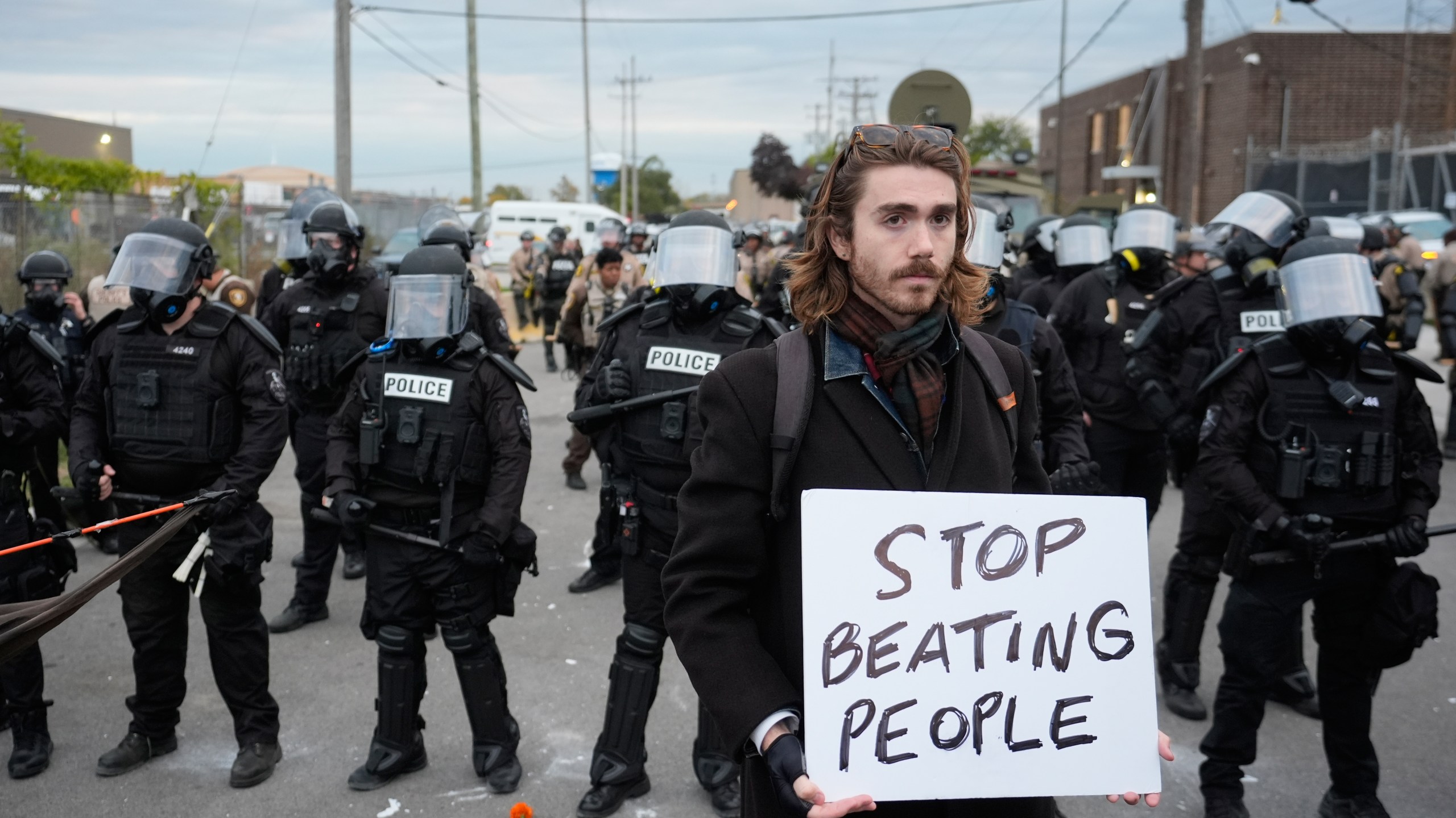A demonstrator holds a sign reading "STOP BEATING PEOPLE" near a line of law enforcement as protesters gather outside an ICE processing facility in the Chicago suburb of Broadview, Ill., Saturday, Nov. 1, 2025. (AP Photo/Alex Brandon)