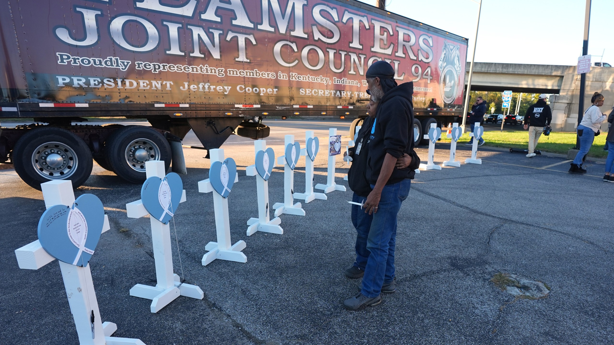 Allen Wilson, right, hugs an attendee after they wrote on crosses for victims during a vigil Thursday, Nov. 6, 2025, in Louisville, Ky., after a UPS plane crashed at Louisville Muhammad Ali International Airport. (AP Photo/Darron Cummings)