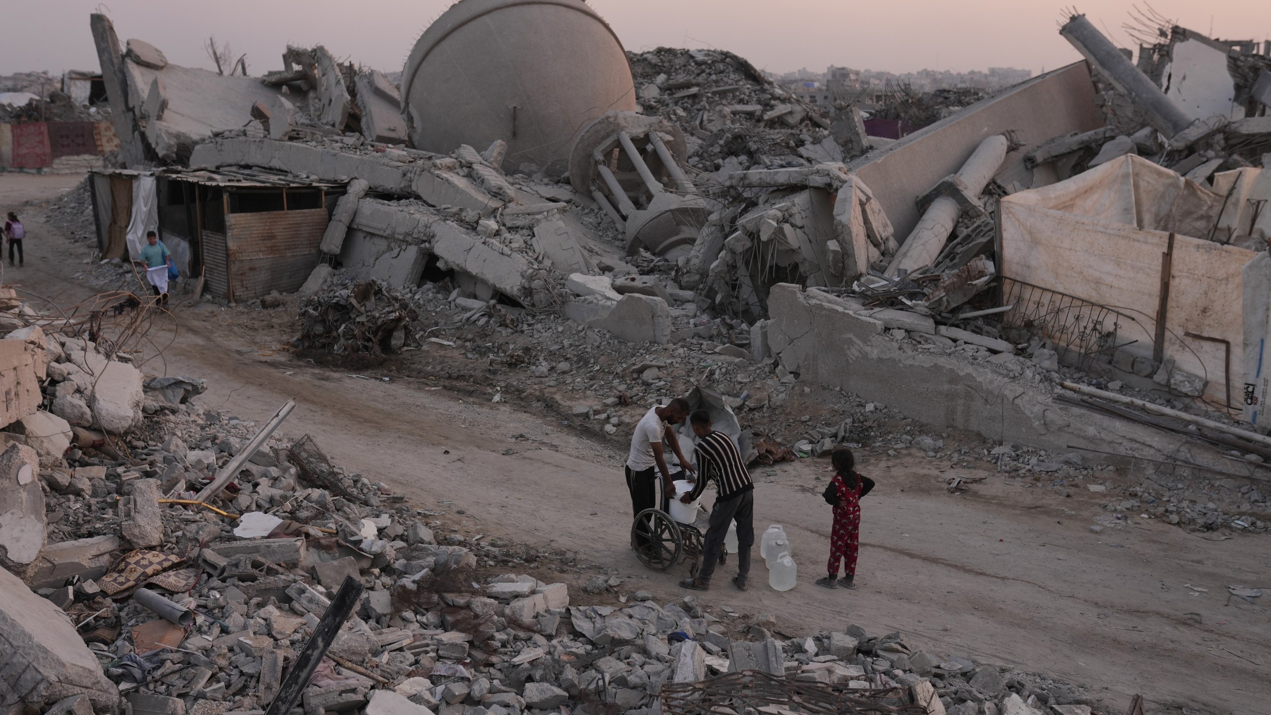 Palestinians carry water through the destruction caused by the Israeli air and ground offensive in Sheikh Radwan neighborhood in Gaza City, Monday, Nov. 10, 2025. (AP Photo/Jehad Alshrafi)
