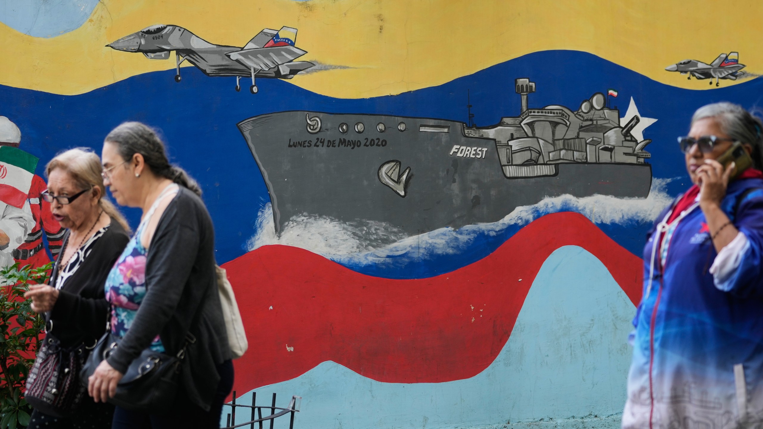 Pedestrians walk past a mural featuring a Venezuelan warship and aircraft in downtown Caracas, Venezuela, Tuesday, Nov. 11, 2025. (AP Photo/Ariana Cubillos)