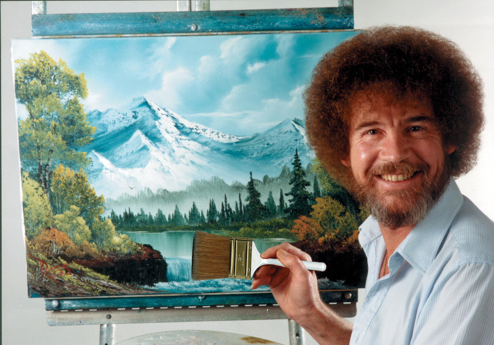 In this undated photo provided by Bob Ross Inc., Bob Ross poses for a photo in front of one of his paintings. (Bob Ross Inc. via AP)