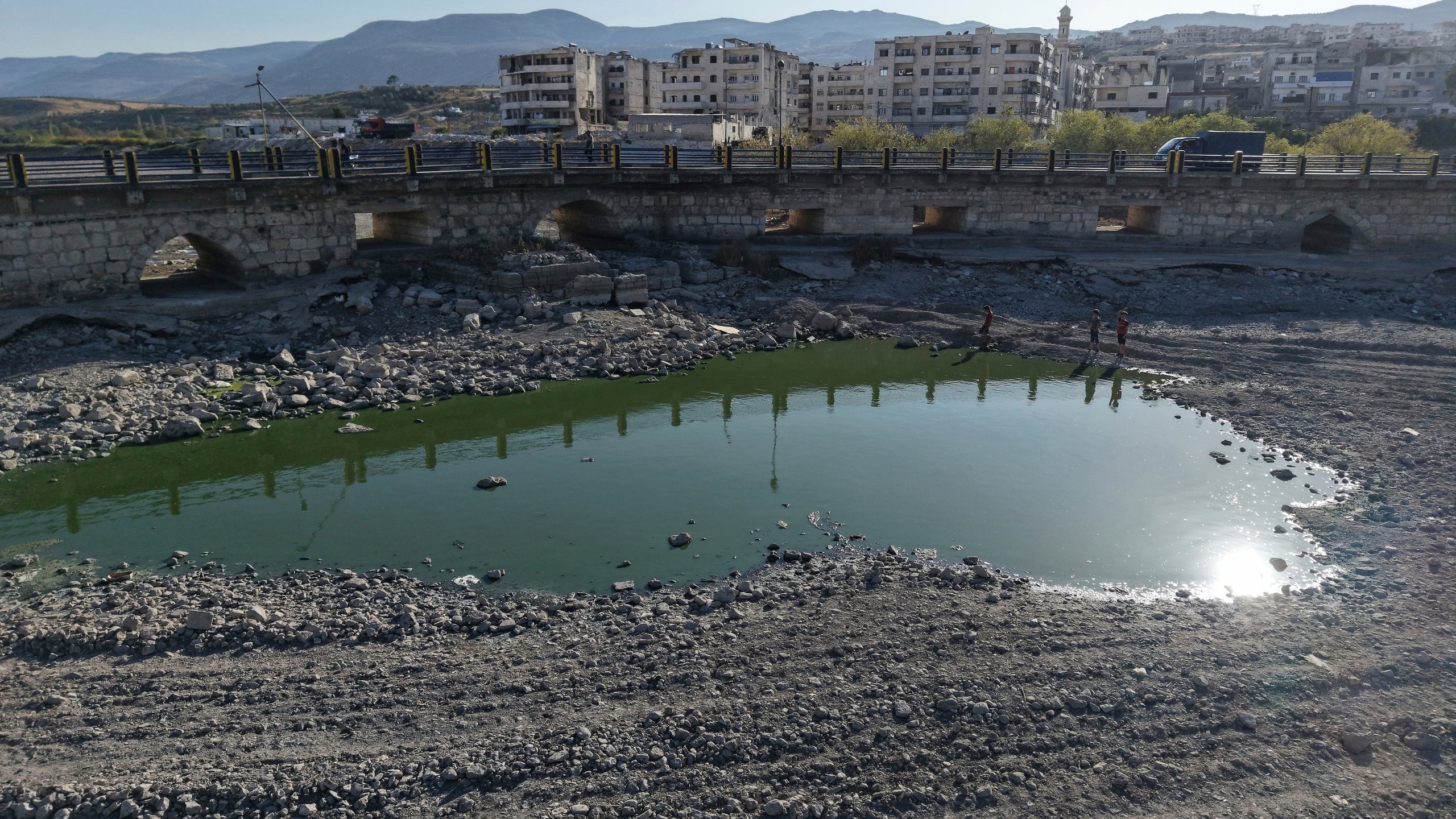 FILE - Boys stand next to the dried up Orontes River, the result of a drought following heat waves and a winter with very little precipitation, in Jisr al-Shughur, west of Idlib, Syria, Aug. 14, 2025. (AP Photo/Omar Albam, File)