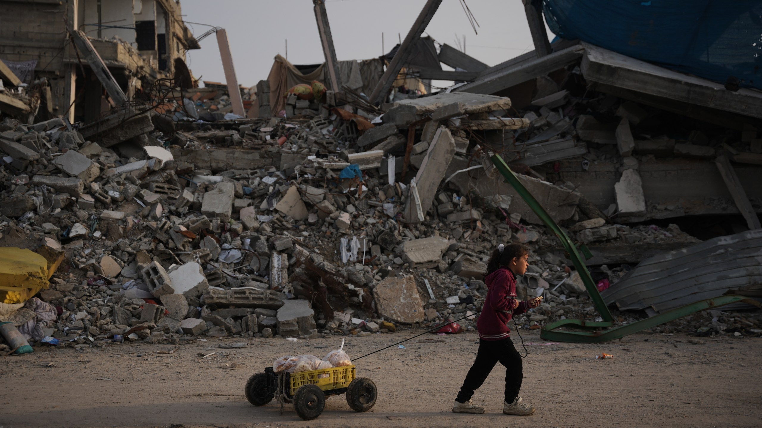 A girl carries bread as she walks past destruction left by Israeli air and ground operations in Gaza City Saturday, Nov. 29, 2025. (AP Photo/Abdel Kareem Hana)