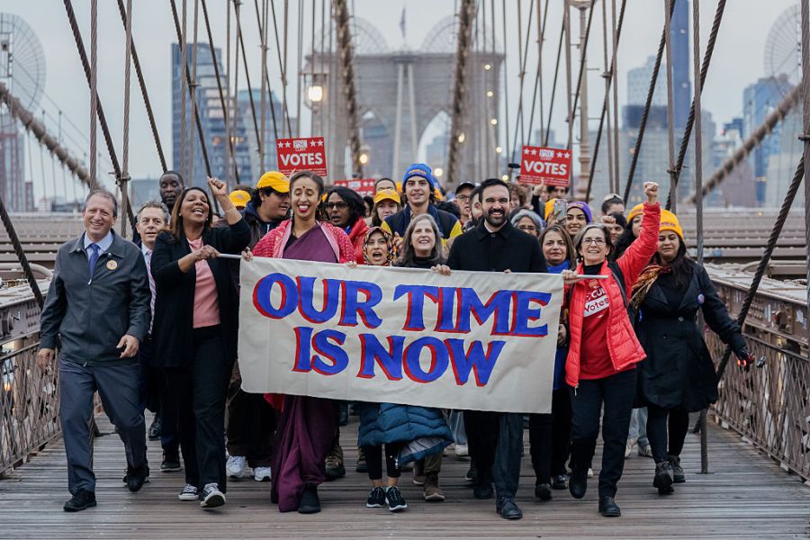 a group of people cheering holding a sign reading OUR TIME IS NOW