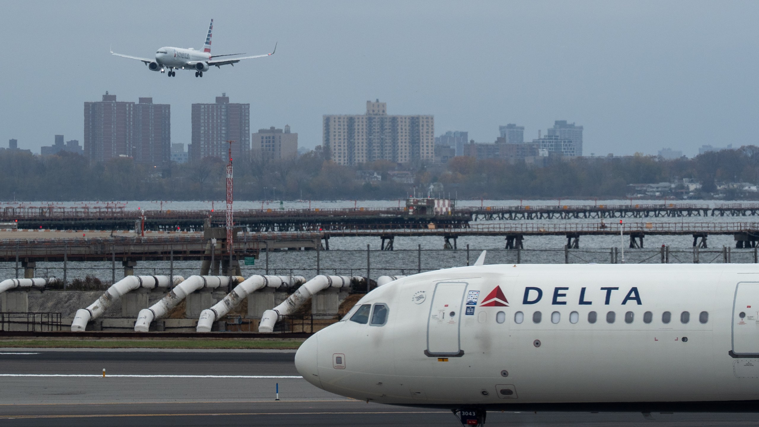 An American Airlines flight lands as a Delta Air Lines plane taxis at LaGuardia Airport (LGA) in the Queens borough of New York, Sunday, Nov. 9, 2025. (AP Photo/Adam Gray)