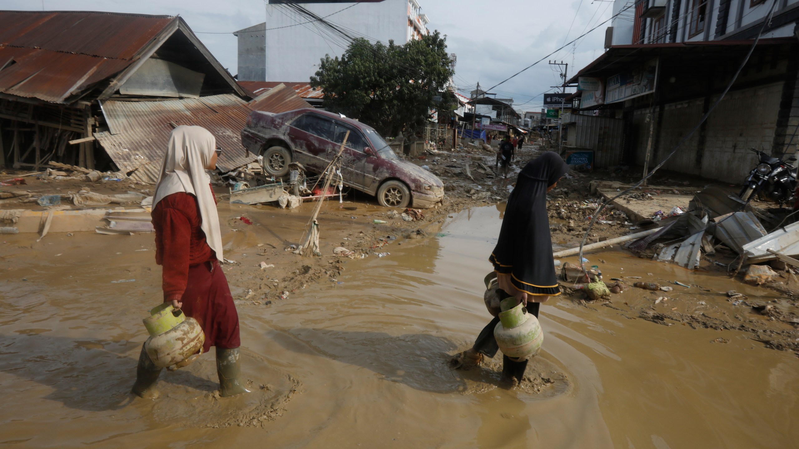 FILE - Survivors walk past the wreckage of a car at an area affected by flash flooding in the aftermath of Cyclone Senyar in Aceh Tamiang, on Sumatra Island, Indonesia, Thursday, Dec. 4, 2025. (AP Photo/Binsar Bakkara, File)