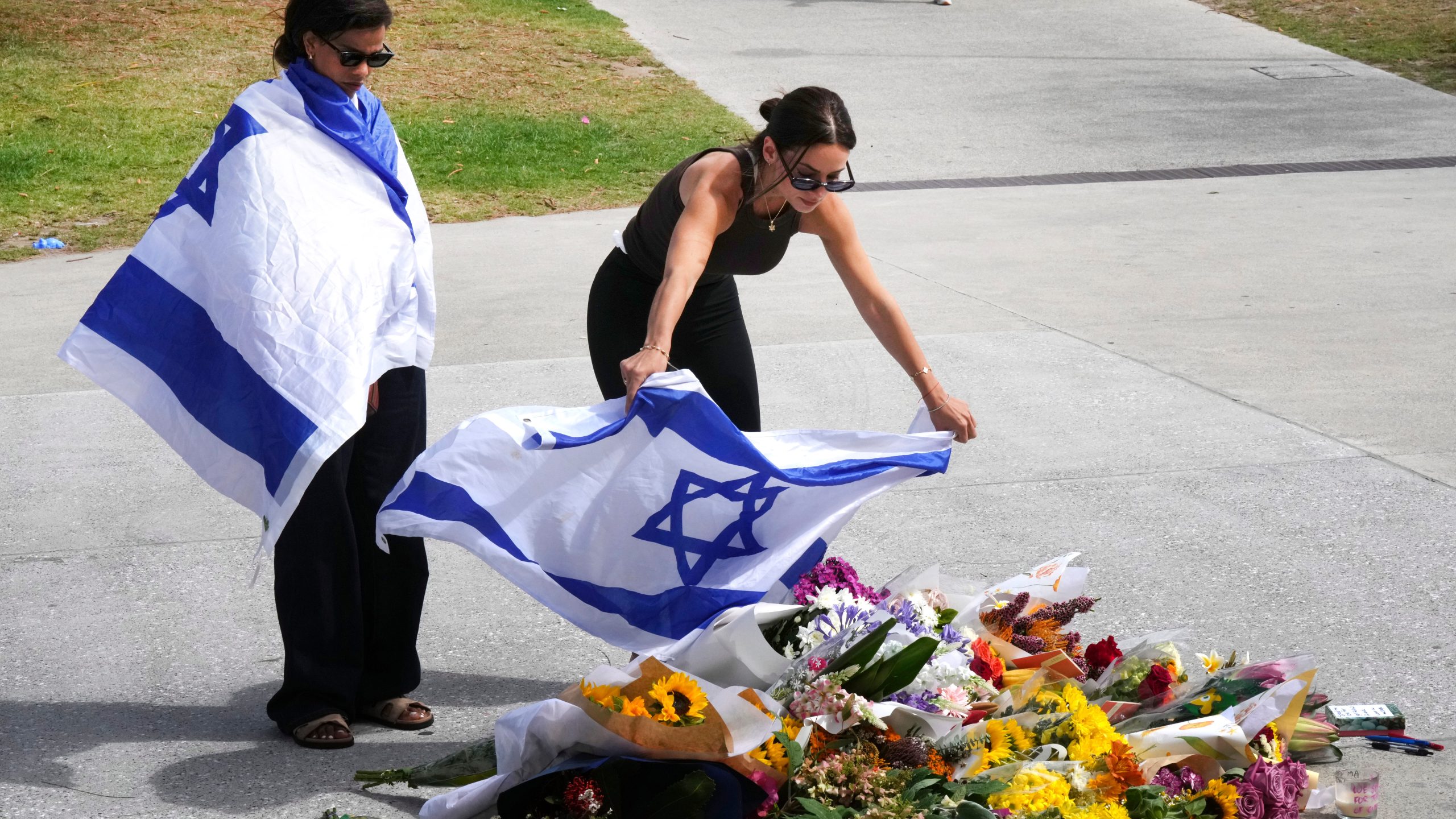 A woman places an Israeli flag over flowers outside Bondi Pavilion at Sydney's Bondi Beach, Monday, Dec. 15, 2025, a day after a shooting. (AP Photo/Mark Baker)