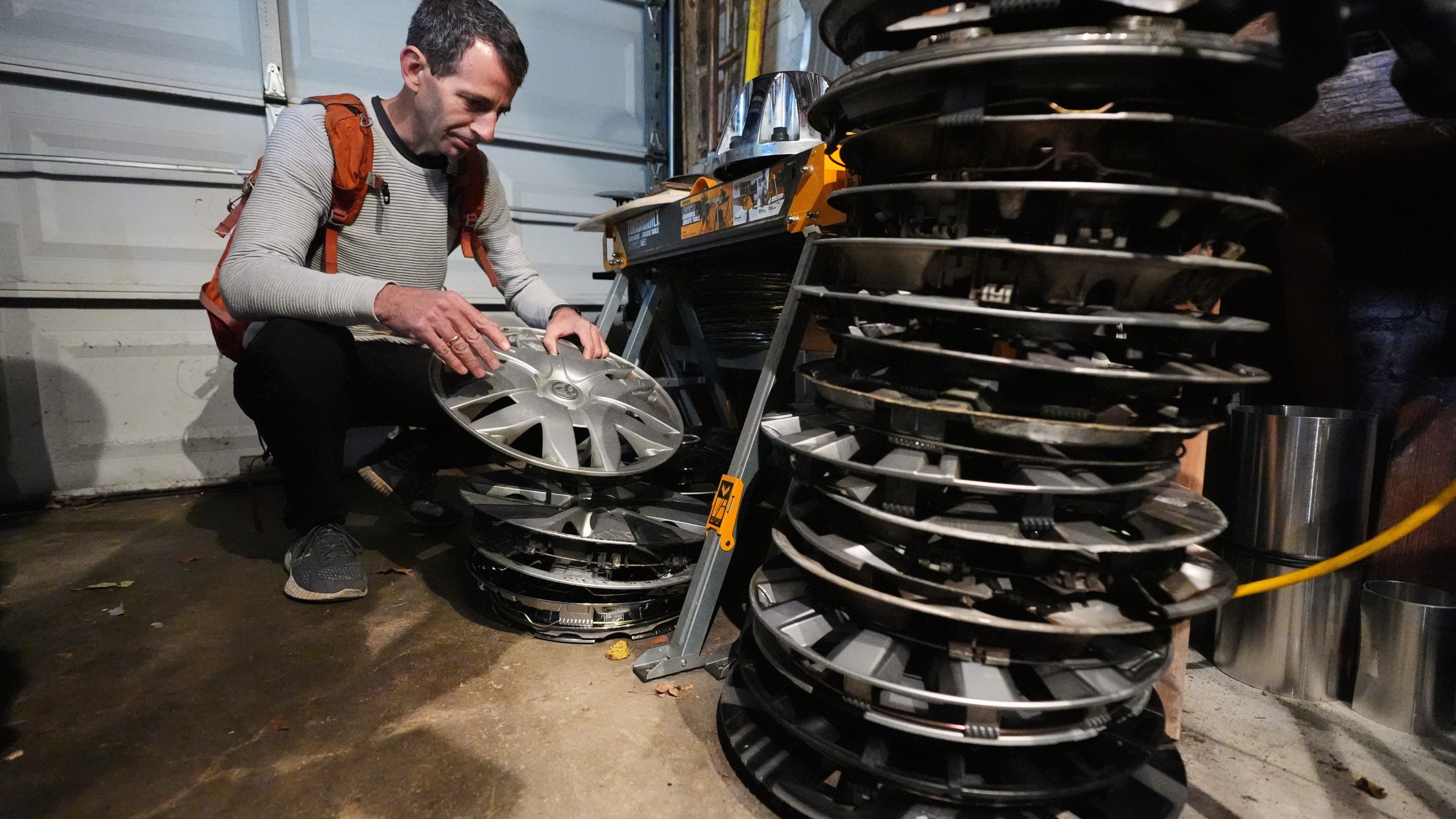 Cyclist Barnaby Wickham sorts through his collection of hubcaps stored in his garage, Thursday, Dec. 11, 2025, at his home in Baltimore. (AP Photo/Stephanie Scarbrough)