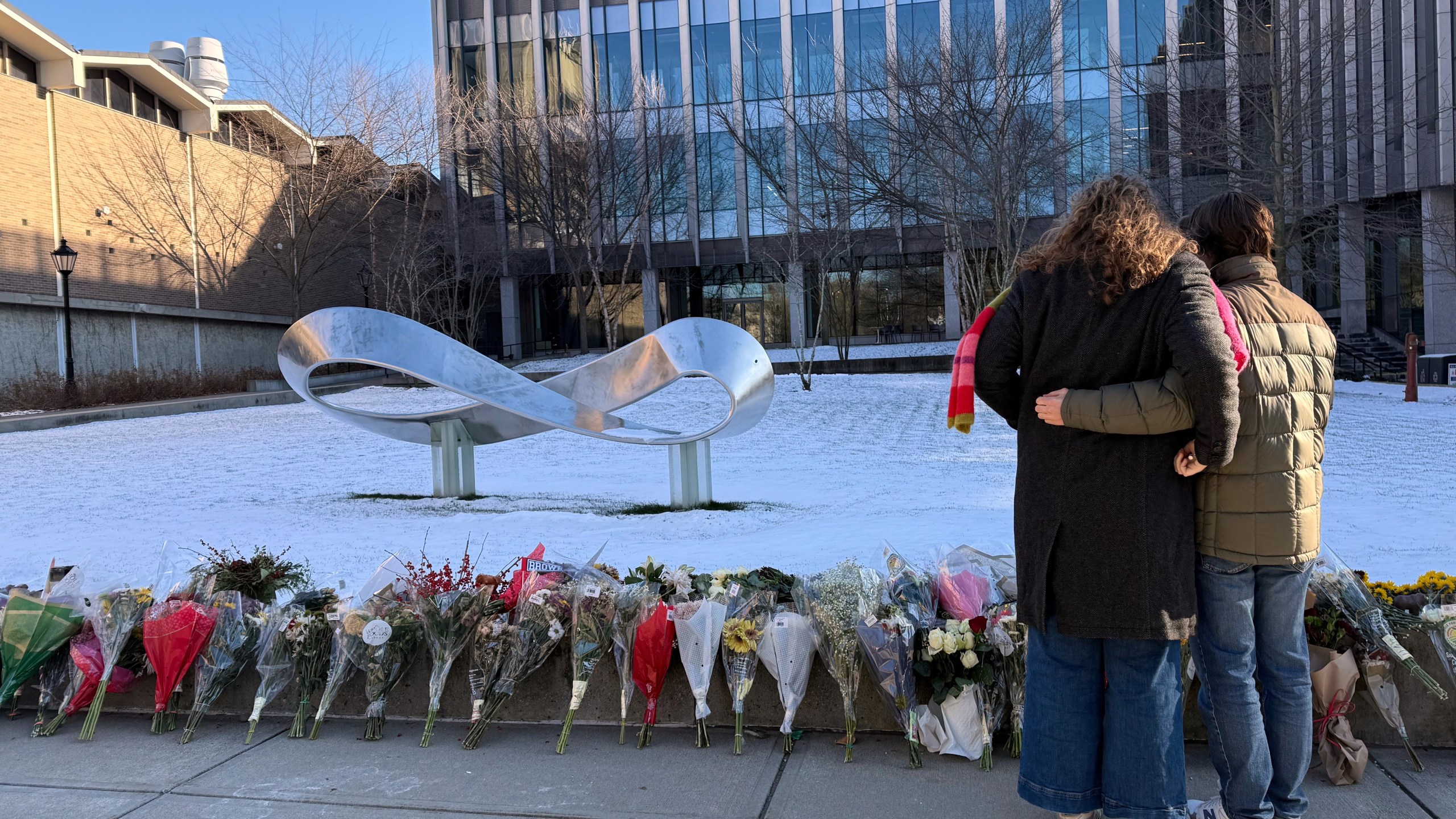 Brown University senior Zoe Kass and her boyfriend return to the engineering building they fled Saturday to leave flowers on Tuesday, Dec. 16, 2025, in Providence, R.I. (AP Photo/Matt OBrien)