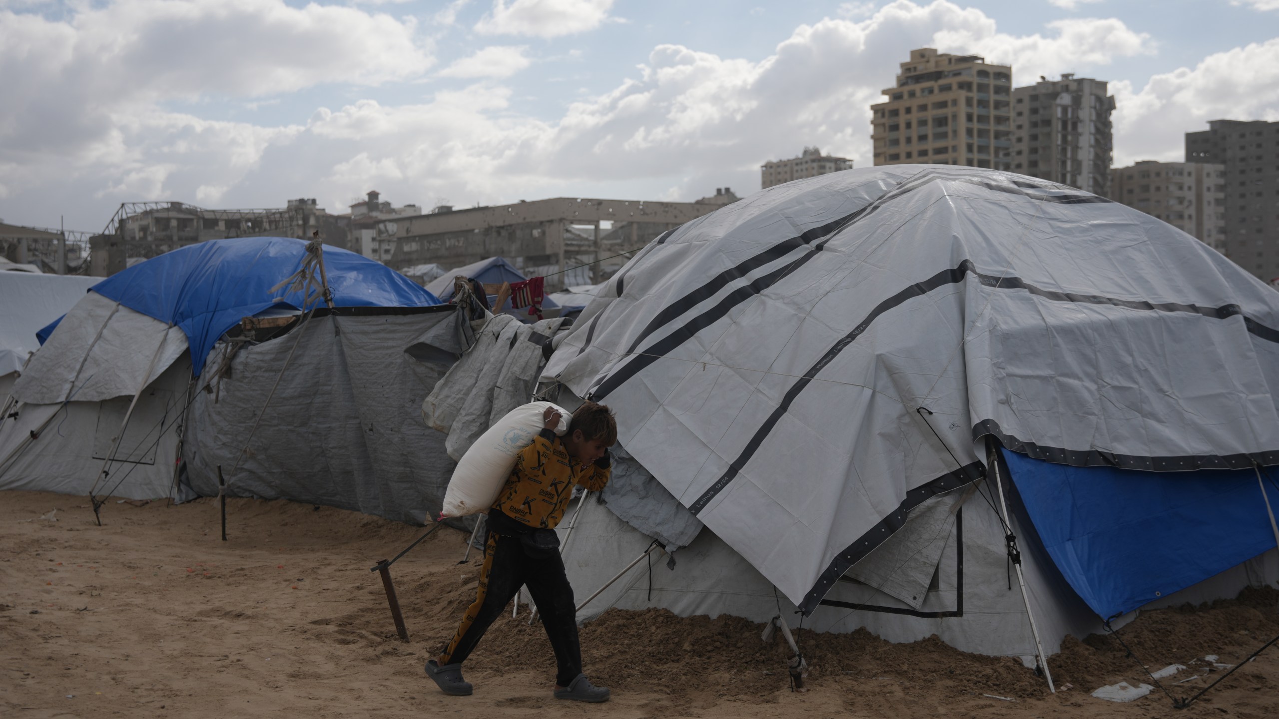 A Palestinian child carries a bag of flour on his back at a makeshift camp on the beach, in Gaza City, Sunday, Dec. 28, 2025. (AP Photo/Jehad Alshrafi)