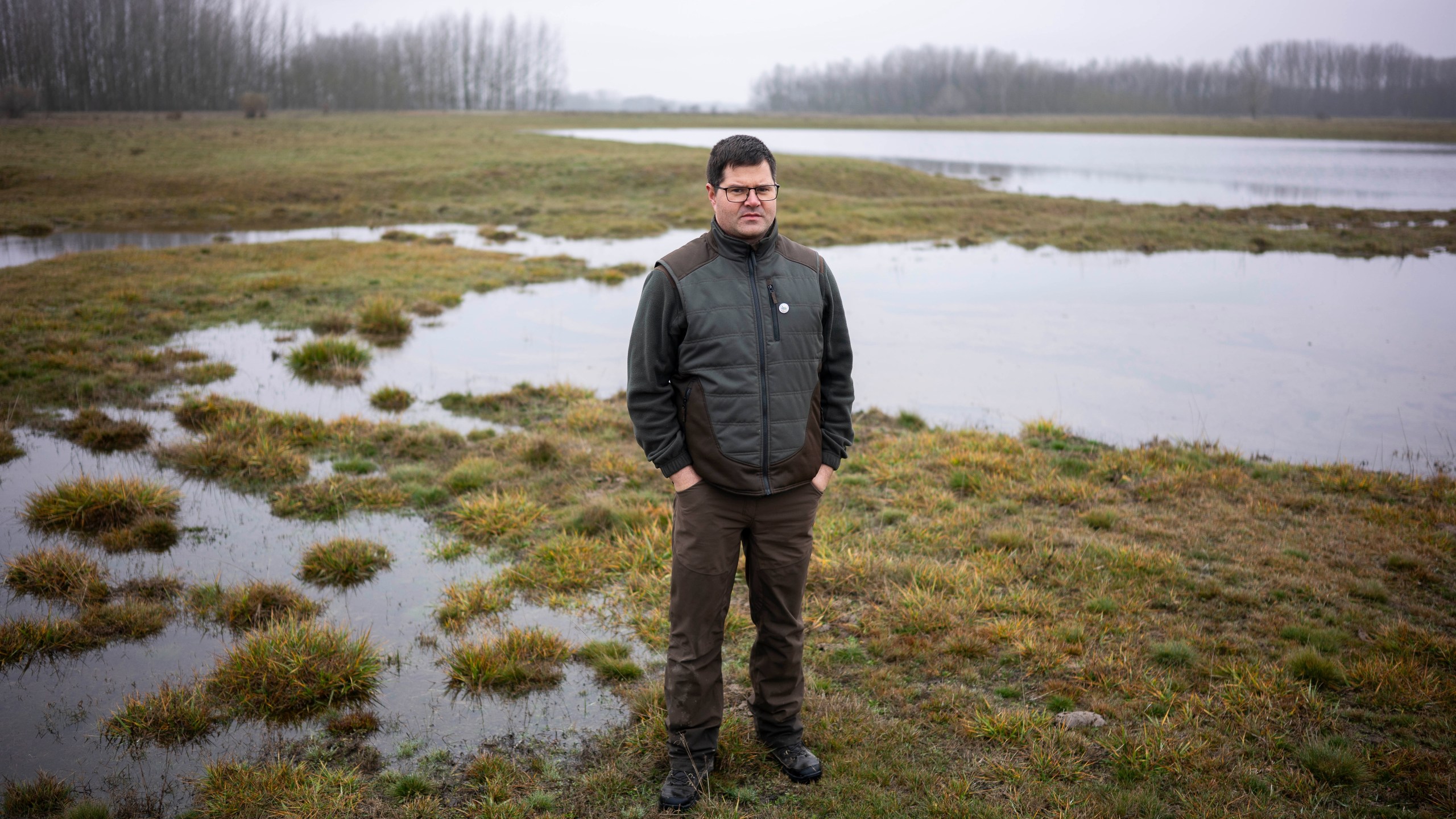 Oszkár Nagyapáti, farmer and member of the volunteer water guardians group, poses for a photo with an artificial lake in Kiskunmajsa, Hungary, Tuesday, July 29, 2025. (AP Photo/Denes Erdos)