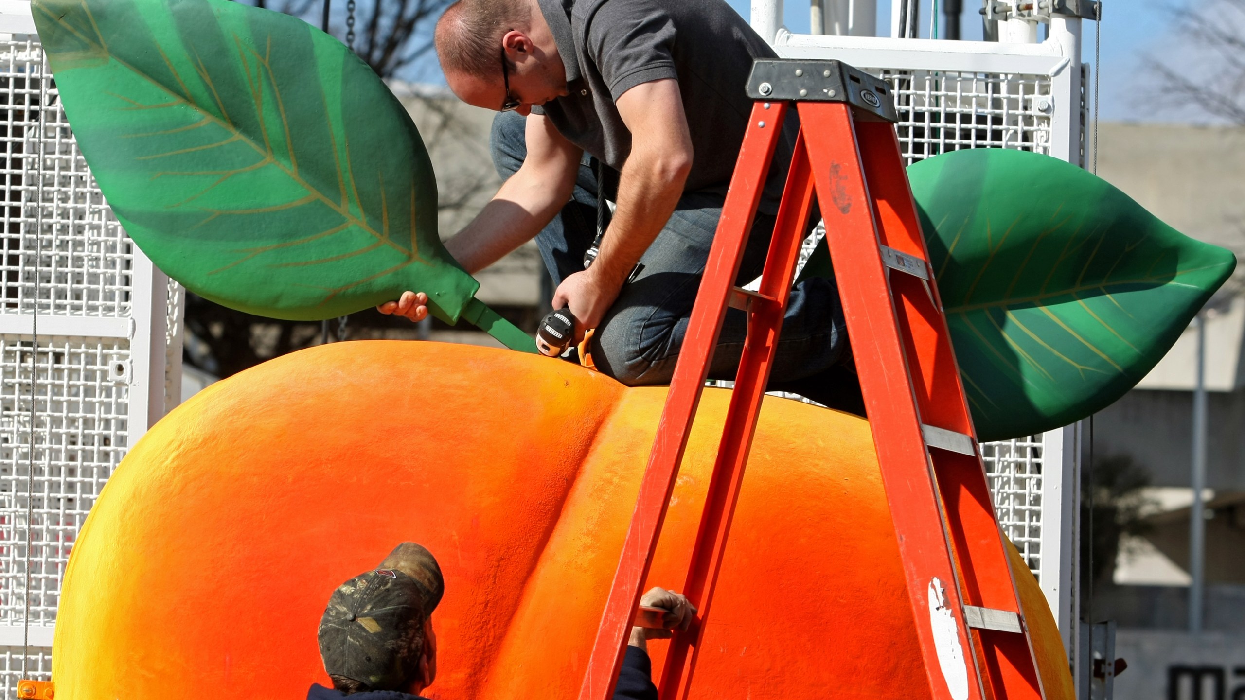FILE - Gary Seputis, top, and Clint Hornsby, employees of Entertainment Design Group, work on attaching two leaves to the fiberglass and foam Peach in preparation for the 2012 Peach Drop at Underground Atlanta, Friday, Dec. 30, 2011, in Atlanta. ( Jason Getz/Atlanta Journal-Constitution via AP, File)