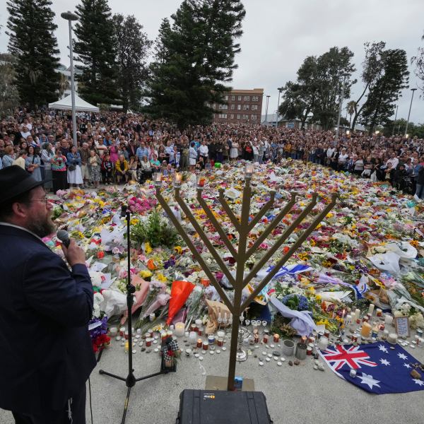 A rabbi stands in front of a large, gold menorah as a memorial for the Bondi Beach shooting victims take place