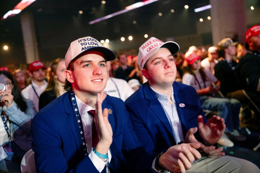 Turning Point USA supporters clap in the crowd wearing MAGA hats