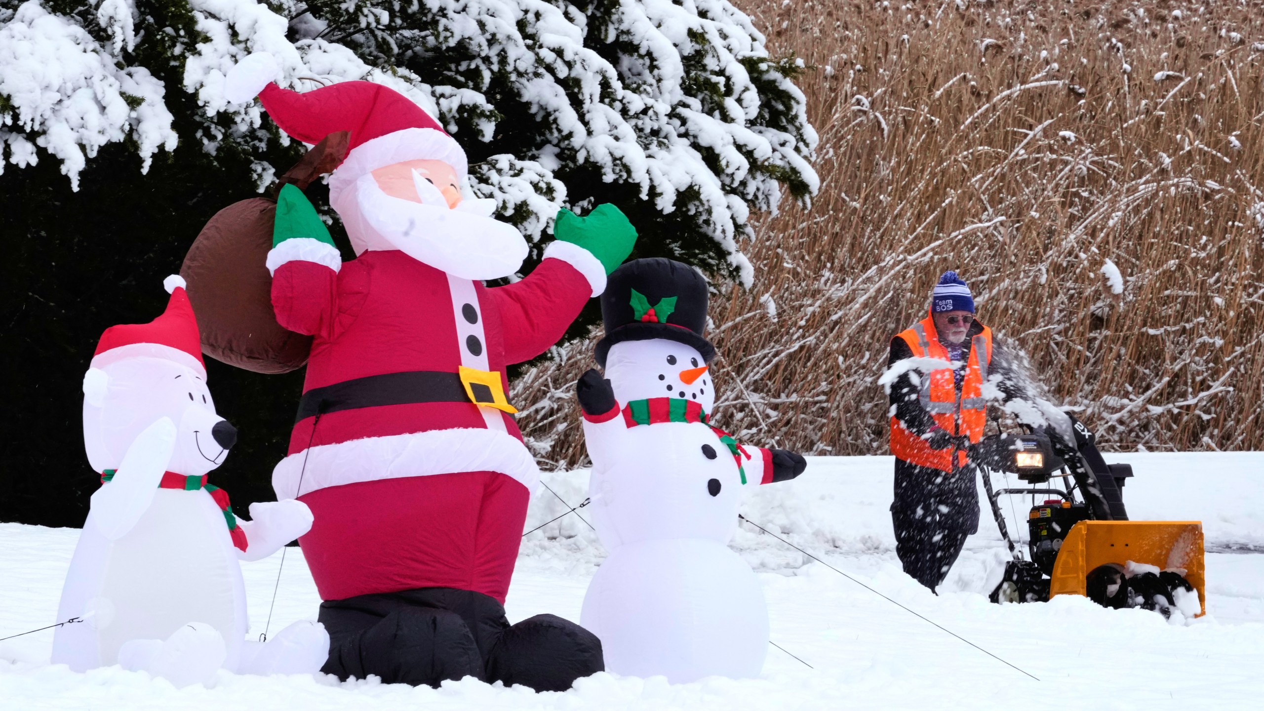 Man passes inflatable snowman while removing snow with snowblower.